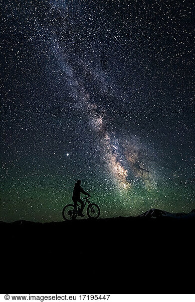 Silhouette cyclist with bicycle on mountain against star field