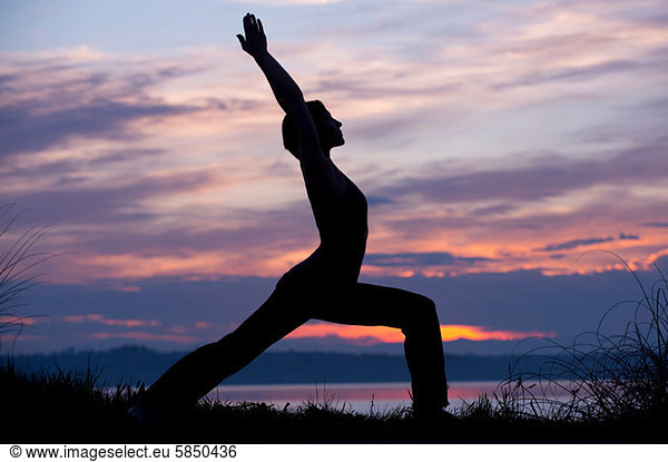 Silhouette der Frau in Krieger-Yoga-Pose bei Sonnenuntergang