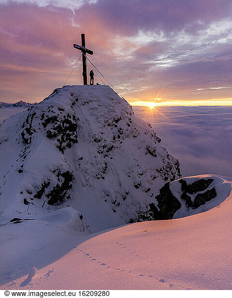 Silhouette einer Frau  die den stimmungsvollen Sonnenuntergang am Kreuz auf dem Gipfel des Aggensteins bewundert