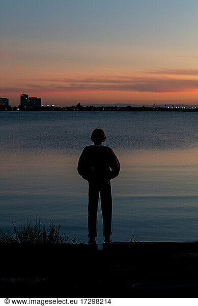 Silhouette einer jungen Person  die bei Sonnenuntergang über die Bucht auf die Stadt blickt