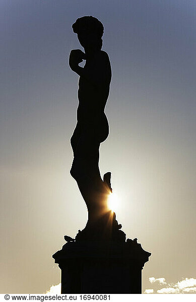 Silhouette einer klassischen Statue mit untergehender Sonne dahinter.