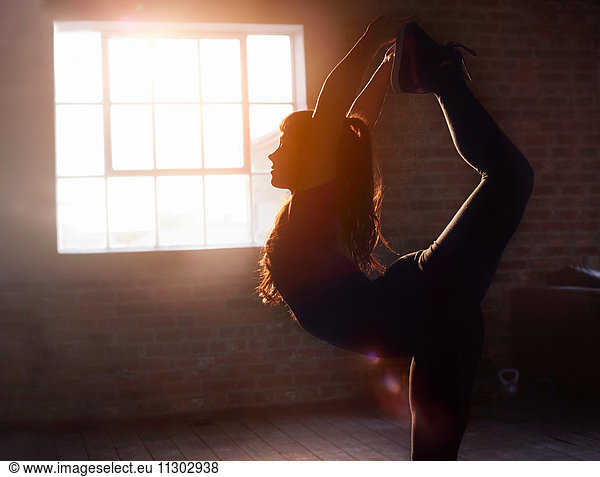 Silhouette female dancer stretching practicing yoga king dancer pose in studio