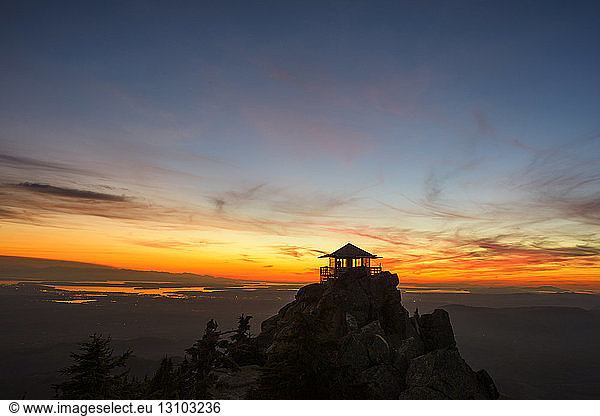 Silhouette fire lookout tower on mountains against sky during sunset