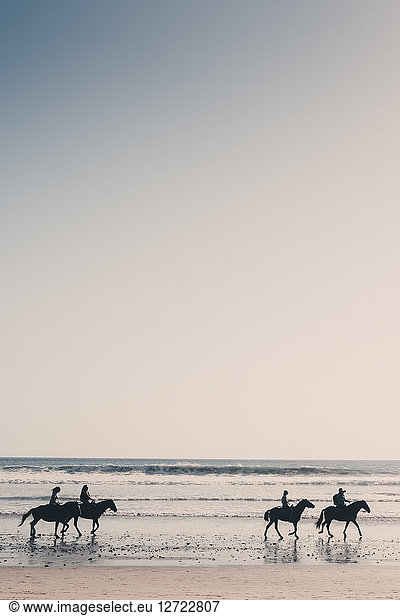 Silhouette friends riding horses at beach against clear sky during sunset
