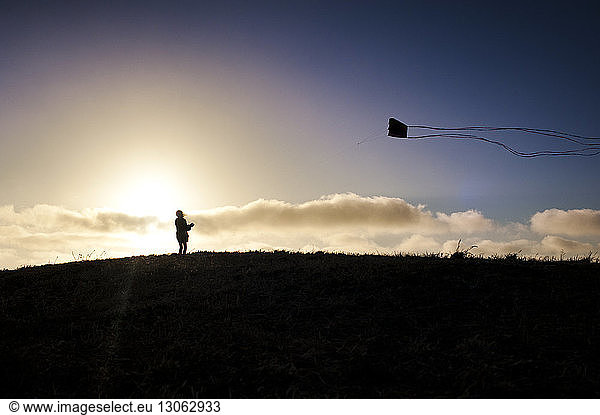 Silhouette girl flying kite on field during sunset