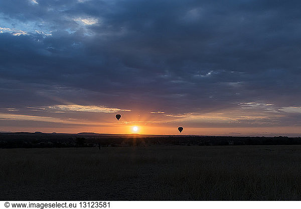 Silhouette hot air balloons flying over landscape against stormy clouds at Serengeti National Park during sunset