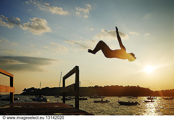 Silhouette man backflipping into sea against sky during sunset