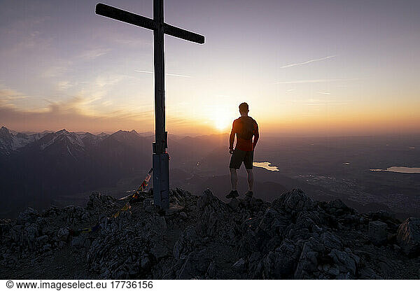 Silhouette man standing by summit cross on mountain