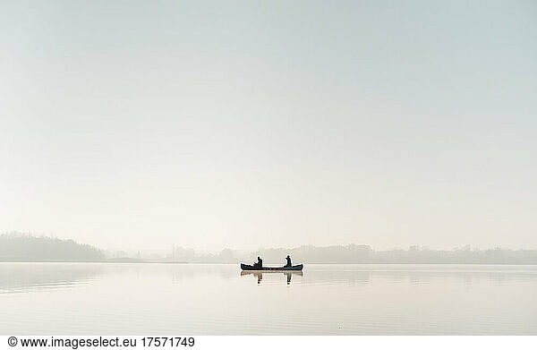Silhouette of a canoe with two people on vast calm water surface