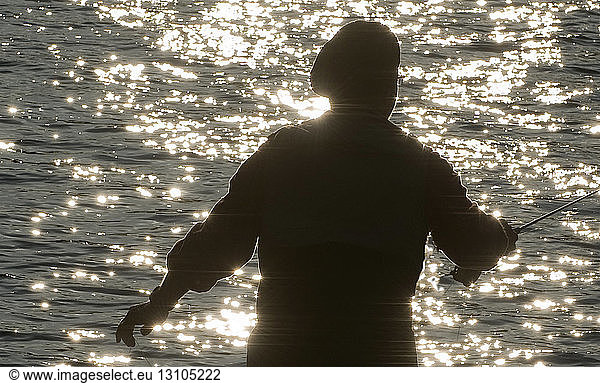 Silhouette of a fly fisherman casting on a river for trout