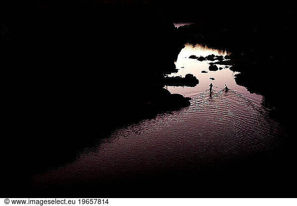 Silhouette of a kayaker and a stand up paddleboarder on calm water at sunset.