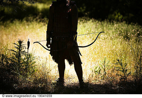 Silhouette of a man with a bow and arrow in a outdoor setting.