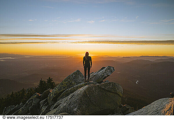 Silhouette of a strong fit woman on a mountain peak at sunset