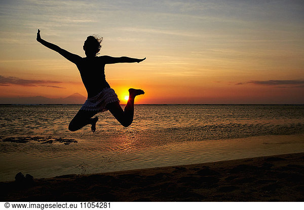 Silhouette of a woman jumping in the air  seen against a sunset sky.