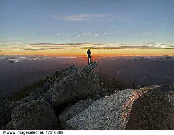 Silhouette of a woman standing on a mountain peak at sunset