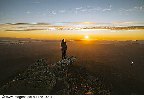 Silhouette of a woman standing on a mountain peak at sunset