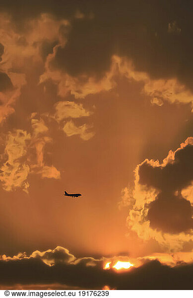 Silhouette of commercial airplane flying against moody sky at sunset