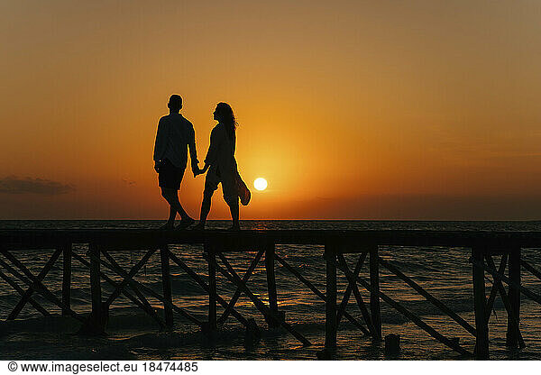 Silhouette of couple walking on pier at sunrise