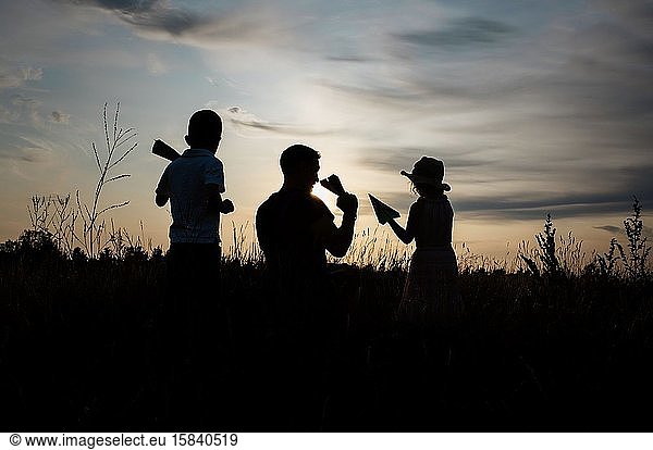 silhouette of father playing with son and daughter outside at sunset