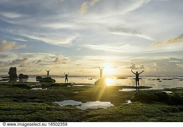 Silhouette of friends arms outstretched at sunset over ocean  Uluwatu  Bali  Indonesia