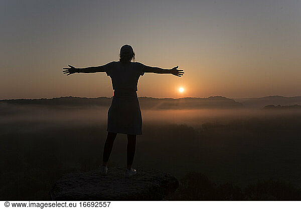 Silhouette of girl at the top of a mountain at sunrise with arms out
