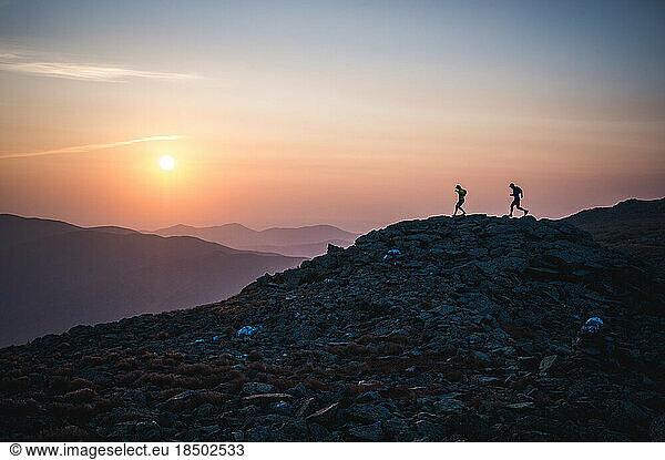 Silhouette of male runners running down ridge at sunrise in mountains