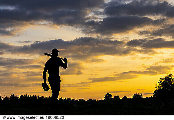 Silhouette of man holding baseball bat at dusk
