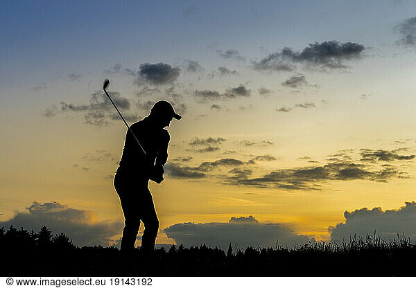 Silhouette of man playing golf at dusk