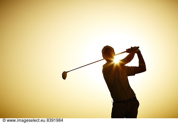 Silhouette of man swinging golf club