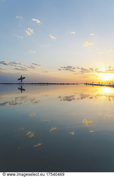 Silhouette of man walking with surfboard at beach with reflection