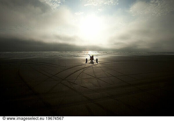 Silhouette of one male kite buggier (kite buggy) rolling down the beach in ominous clouds and unusual light with dark tracks in the sand.