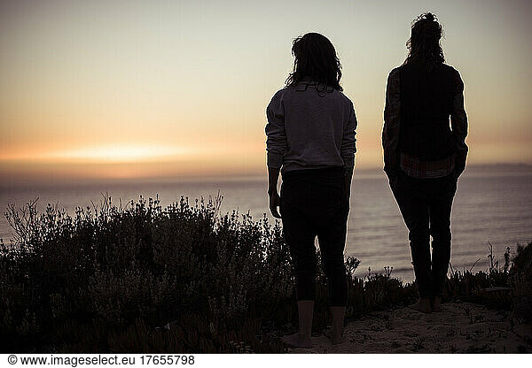Silhouette of two women on ocean cliff watching sunset in Portugal