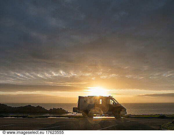 Silhouette of van standing against sun setting over Pointe du Grouin headland