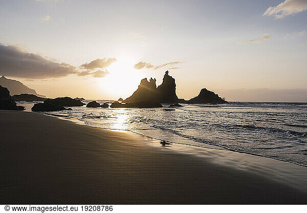 Silhouette of waves and rocks on beach at sunset