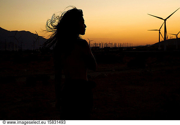 silhouette of woman in front of wind farm at sunset