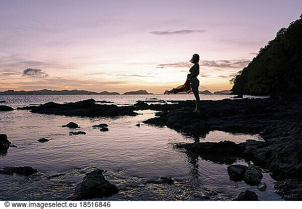 Silhouette of woman standing on beach at dusk