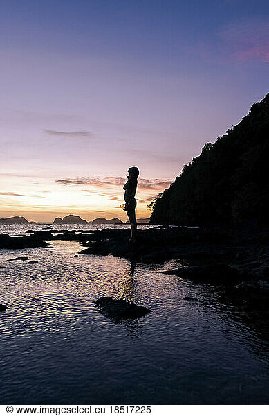 Silhouette of woman standing on rock at beach