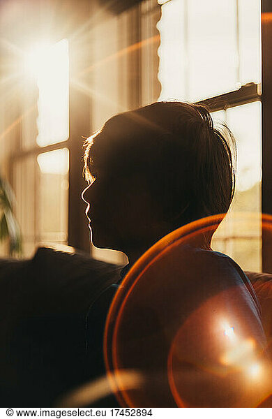 Silhouette of young boy indoors with a large sun flare in the corner.