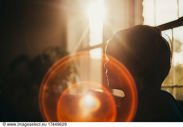 Silhouette of young boy indoors with a large sun flare in the middle.