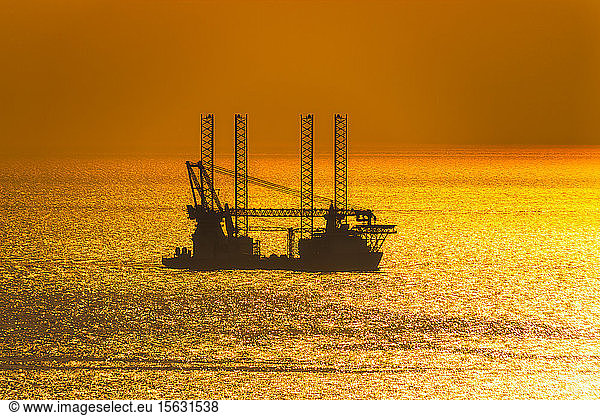 Silhouette offshore wind farm installation vessel sailing off in sea against sky during sunset  West Coast  Scotland  UK