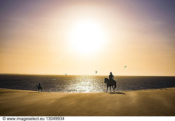 Silhouette von Menschen  die am Strand am Strand gegen den Himmel reiten