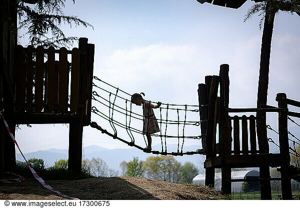 Silhouette young girl standing on kid's rope bridge at playground