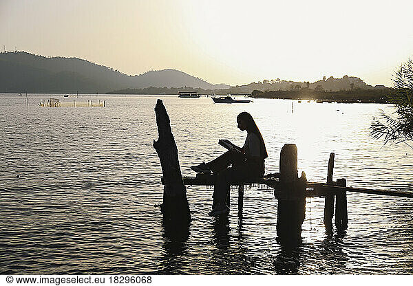 Silhouette young woman sitting on handmade fishing platform in sea