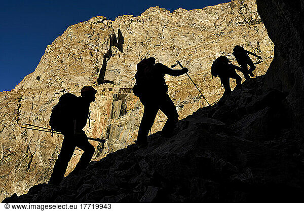 Silhouetted against the sun bathed cliff  the team of four head up the largest of all the scree slopes of rocks we encounted to a third level on the north west facing cliff face  to check out two large cave entrances that had been reported too dangerous to access without rope.