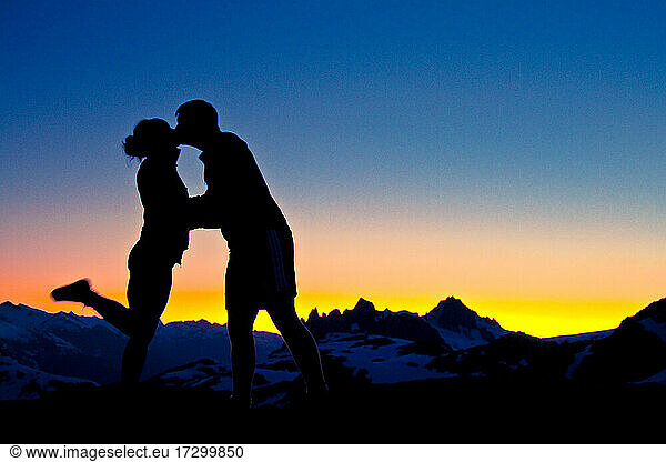 silhouetted Loving couple embrace and kiss on a mountain summit.