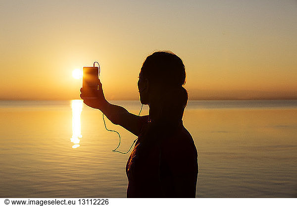 Silhouettenfrau fotografiert den Horizont bei Sonnenuntergang