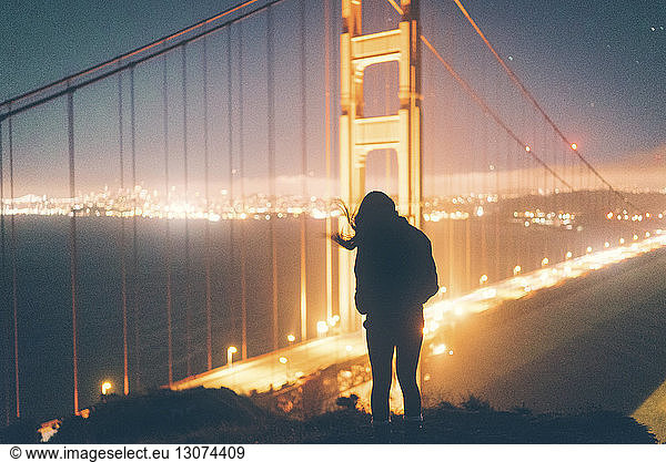 Silhouettenfrau steht nachts vor der beleuchteten Golden Gate Bridge