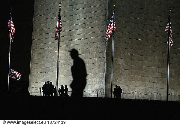 Silhouettes of people as they pass by the high-powered lights that shine on the Washington Monument at night in Washington  DC.