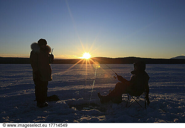 Silhouettes Of People Ice Fishing On Teslin Lake At Sunset  Yukon