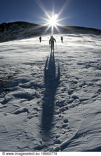 Silhouettes of three people mountaineering / climbing a mountain into the sun.